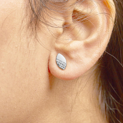 Close-up side view of a white metal teardrop-shaped earring with round white gemstones in a prong setting worn on a model's ear.