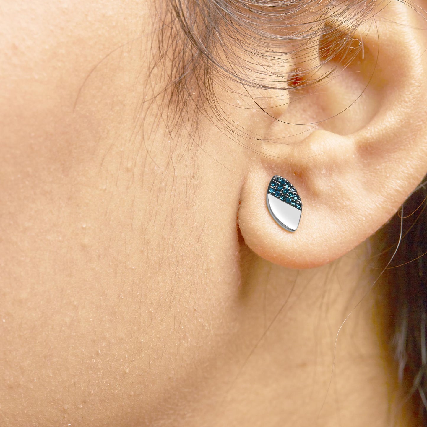 Close-up side view of a white earring on a model's ear featuring a half-covered design with prong-set round blue gemstones.