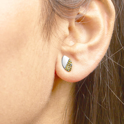 Close-up side view of a white metal earring on a model's ear, featuring a half smooth surface and half covered with small yellow gemstones in a prong setting.