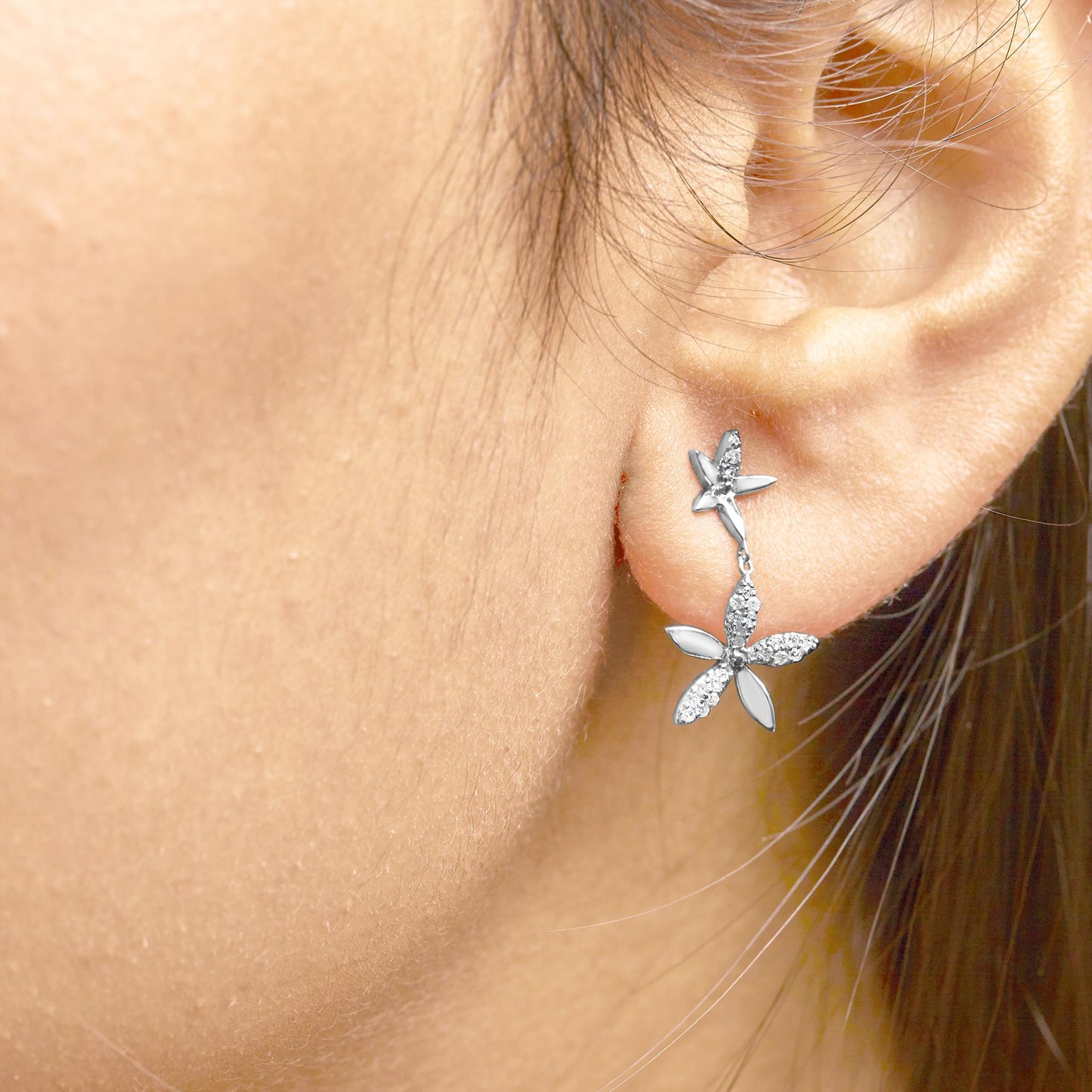 Close-up side view of a model wearing white metal earrings featuring a dual flower design with petals accented by round white gemstones in a prong setting.