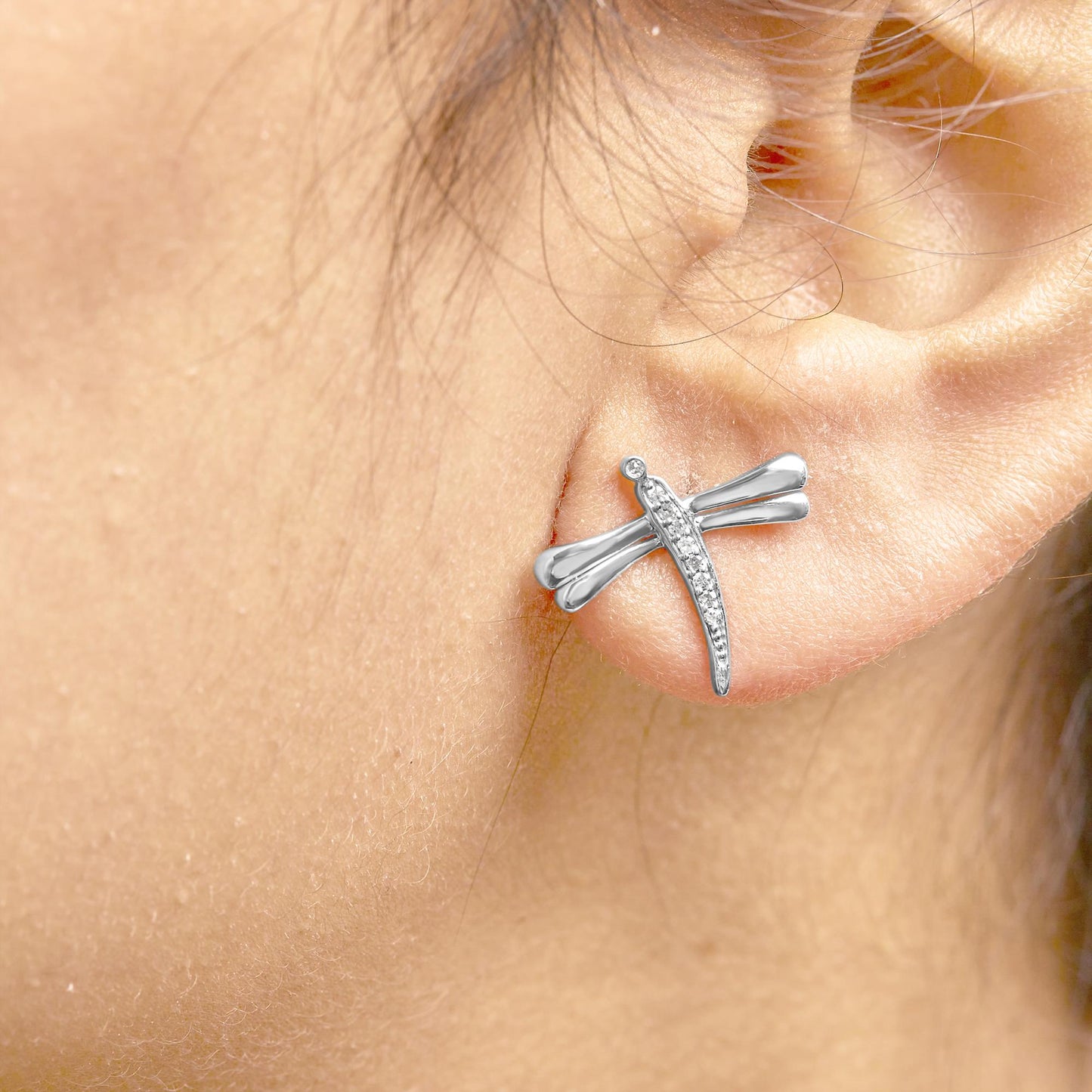 Close-up side view of a white metal dragonfly-shaped earring with round white gemstones in prong settings, worn on a model's ear.