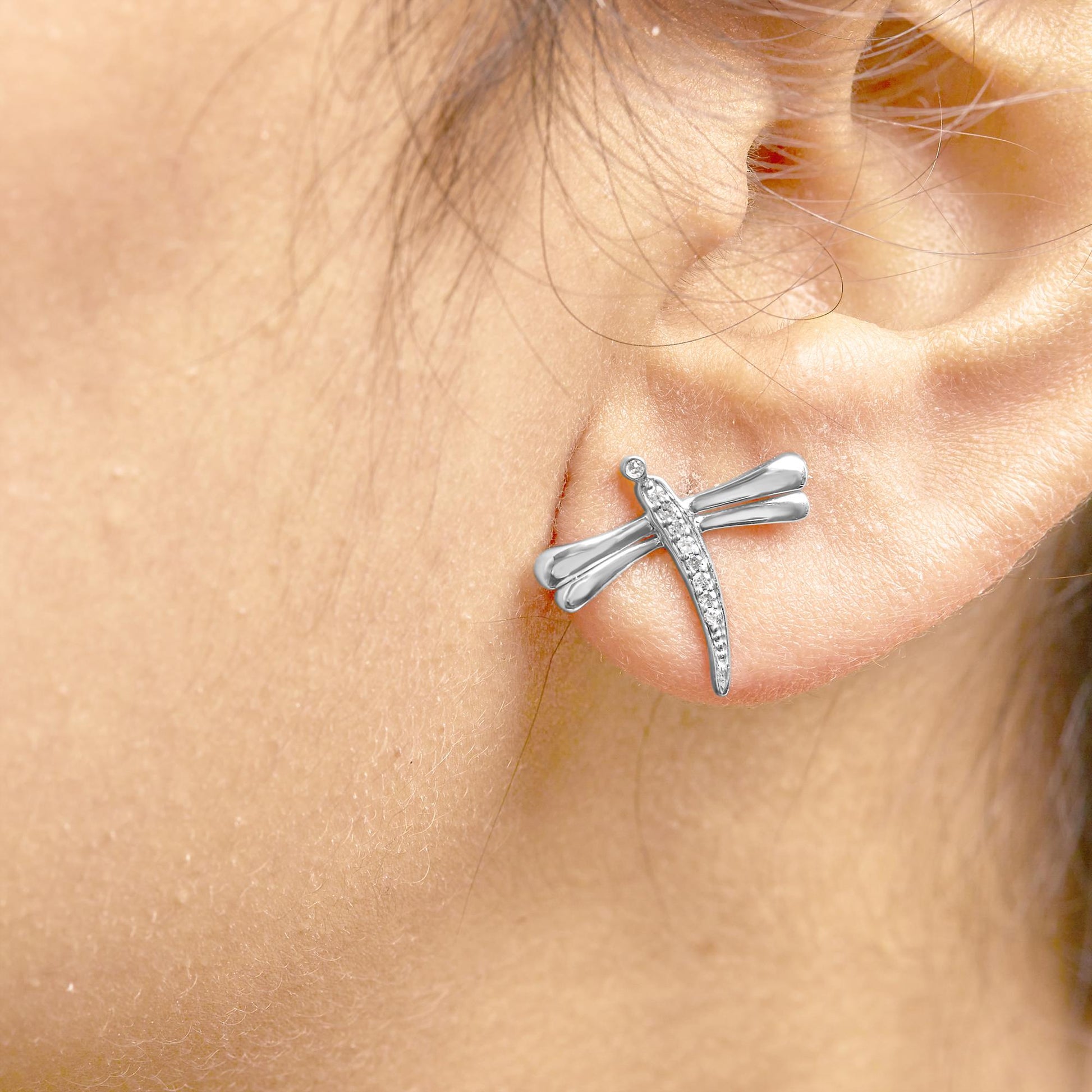 Close-up side view of a white metal dragonfly-shaped earring with round white gemstones in prong settings, worn on a model's ear.