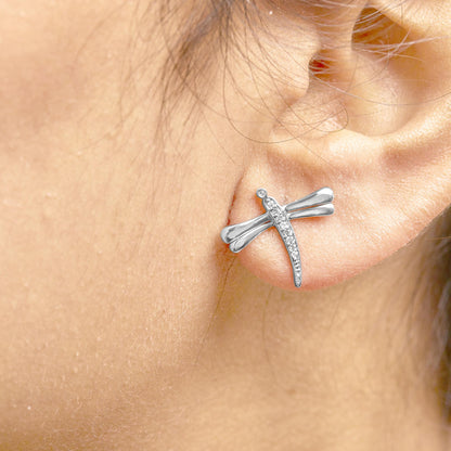 Close-up side view of a white metal dragonfly-shaped earring with round white gemstones in prong settings, worn on a model's ear.