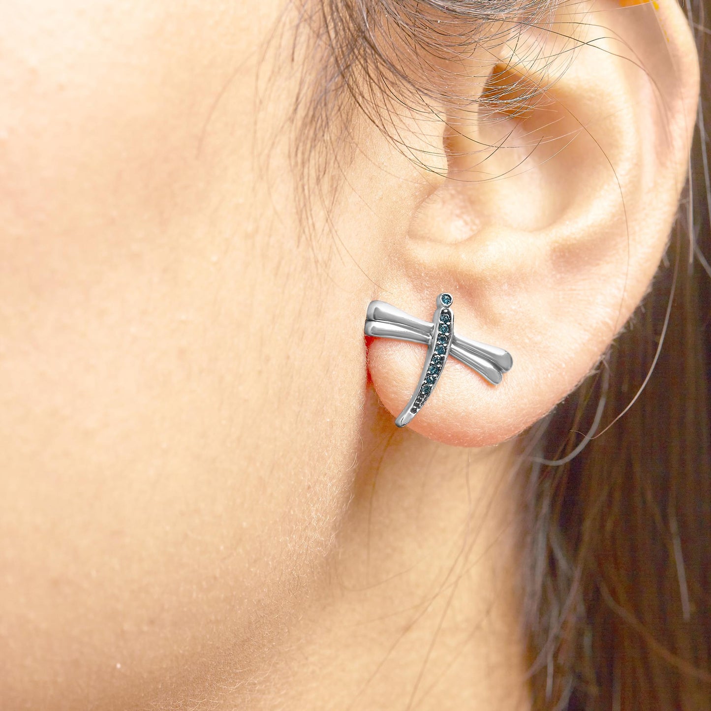 Close-up side view of a white metal earring on a model's ear, designed with a curved bar and round prong-set blue gemstones.
