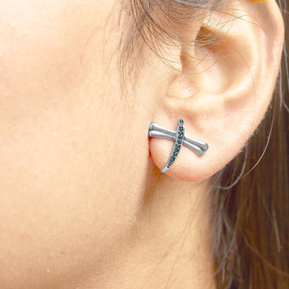 Close-up side view of a white metal earring on a model's ear, designed with a curved bar and round prong-set blue gemstones.