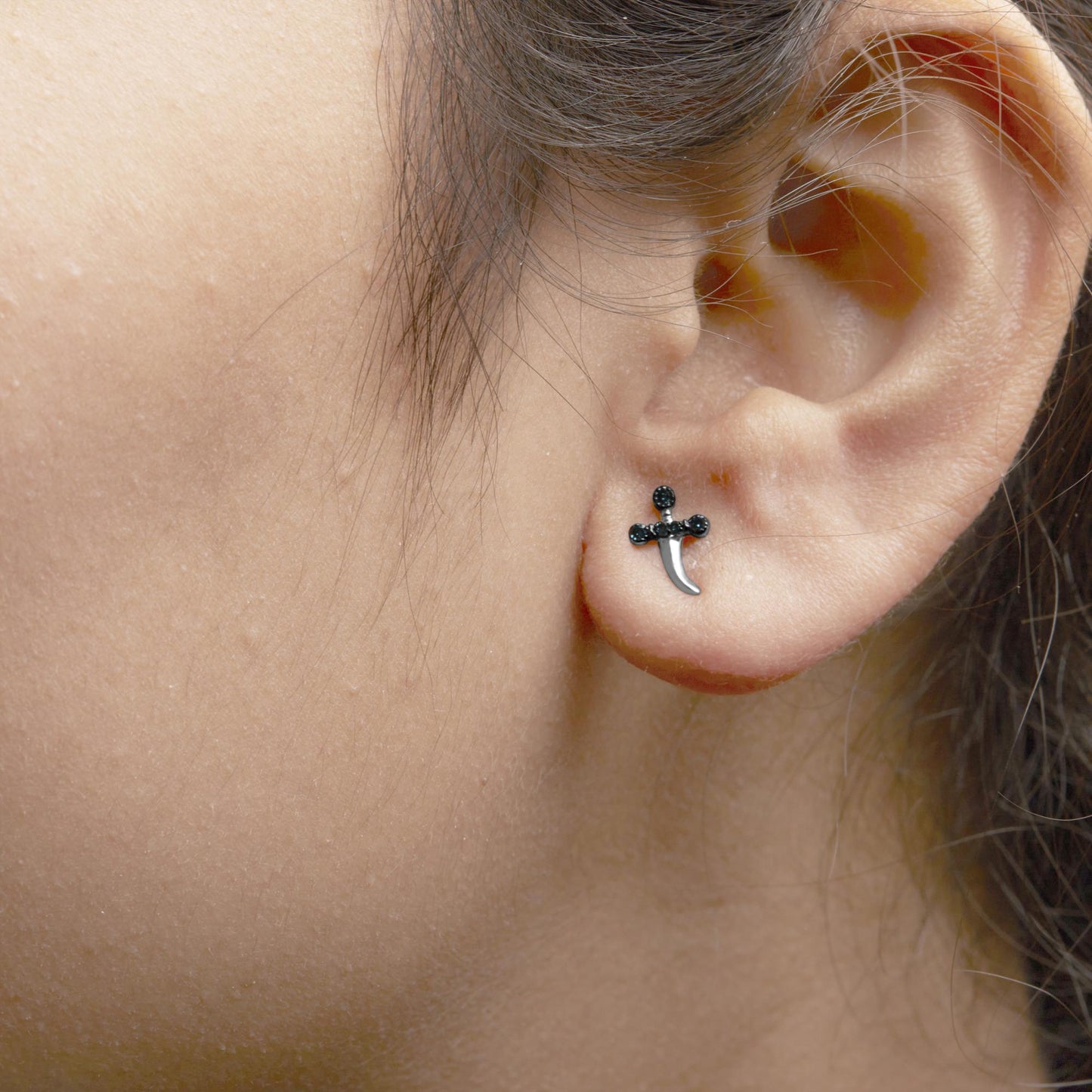 Close-up side view of a white metal earring in the shape of a cross with round blue gemstones in prong settings, worn on a model's ear.