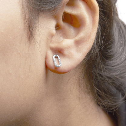 Close-up side view of a white metal earring on a model's ear featuring an elongated oval shape with round white gemstones set in prongs along the lower half.