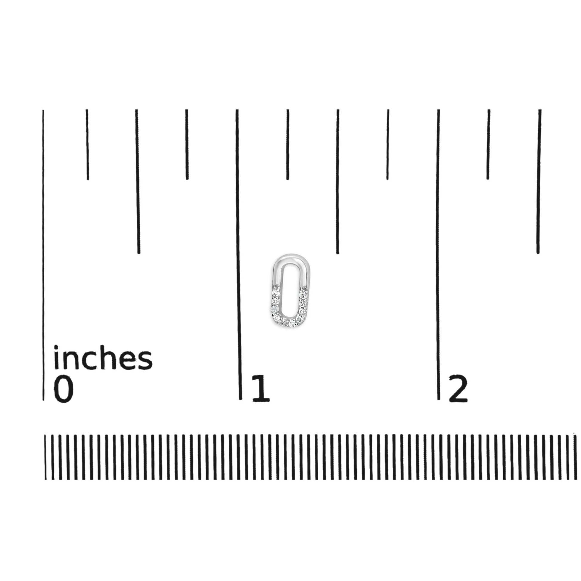 Small white metal oval-shaped earring with round white gemstones in prong setting on the lower half, shown on a ruler for size reference from a top-down angle.