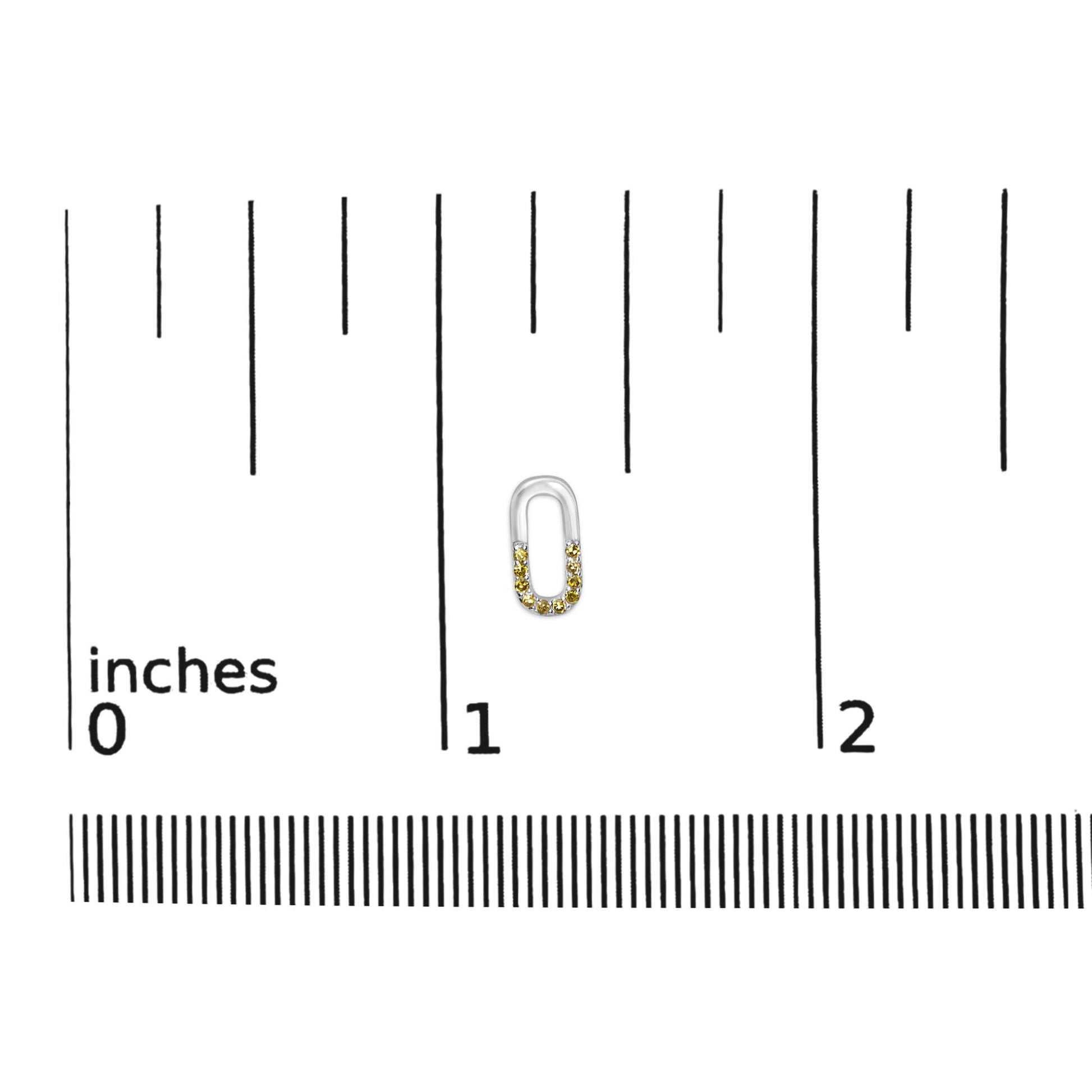 Close-up front view of a white metal earring shaped like an elongated oval with yellow and white round prong-set gemstones, placed on a ruler for size reference.