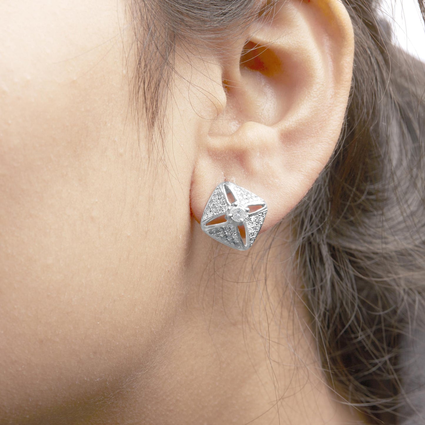 Close-up side view of white metal square-shaped earring with a central round white gemstone and numerous smaller round white gemstones, worn on a model's ear.