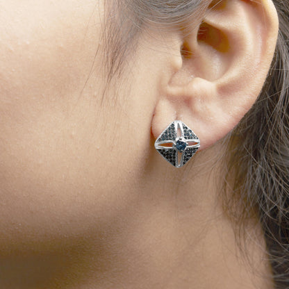 Close-up side view of white metal stud earring on a model's ear featuring blue round gemstones in prong settings, with one larger central gemstone and multiple smaller gemstones arranged around it.