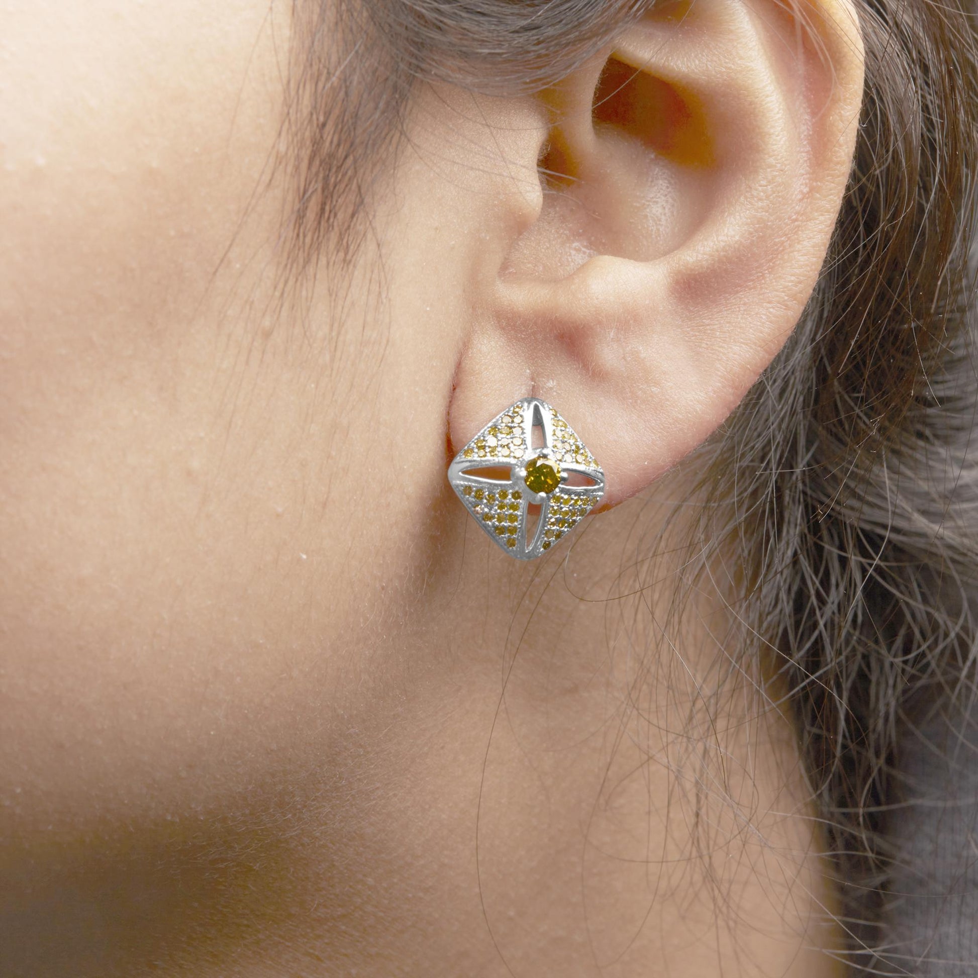 Close-up side view of a white metal earring with a square shape, featuring a central round yellow gemstone and multiple smaller round yellow gemstones set in prongs, worn on a model's ear.