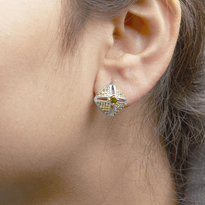 Close-up side view of a white metal earring with a square shape, featuring a central round yellow gemstone and multiple smaller round yellow gemstones set in prongs, worn on a model's ear.
