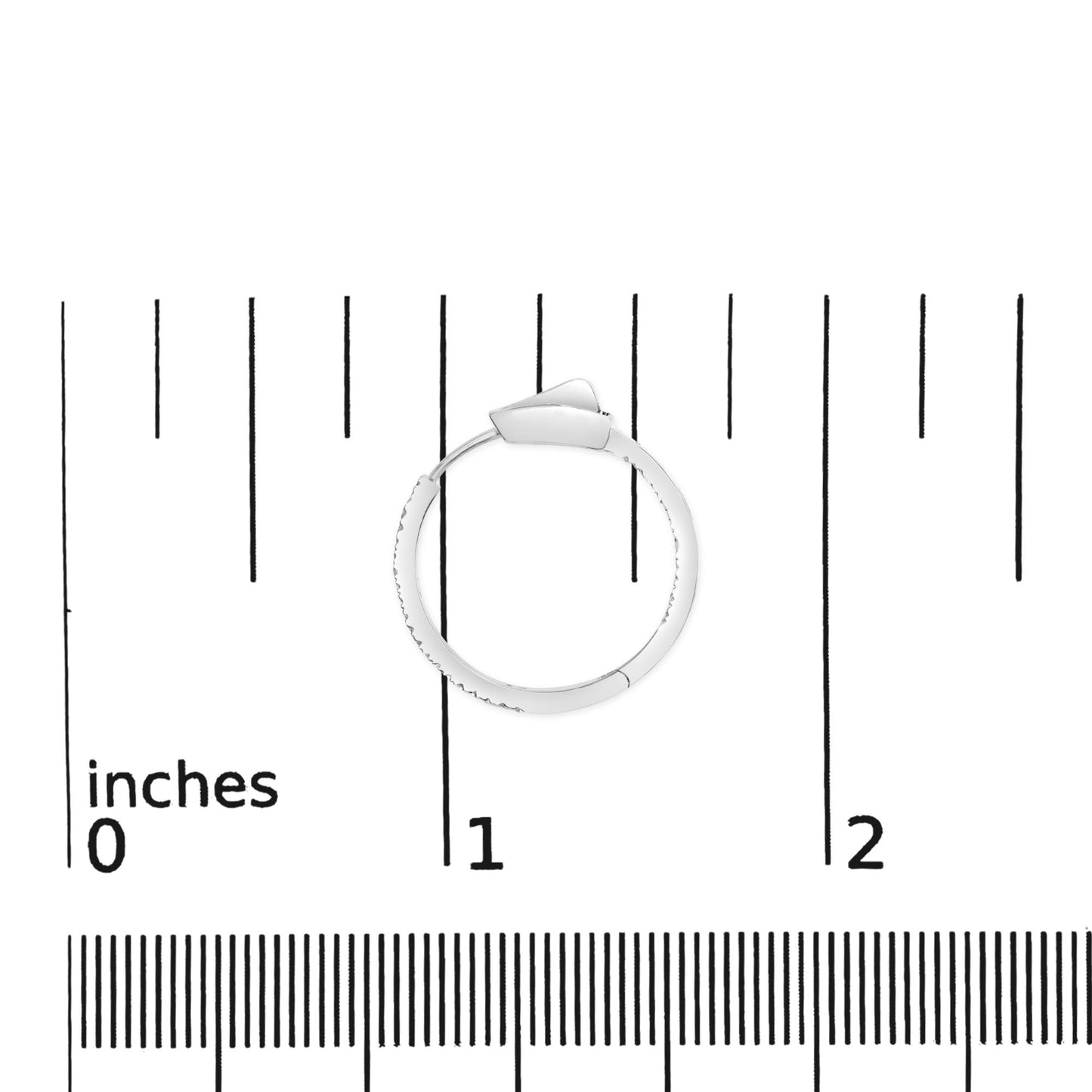 Top-down view of a white metal hoop earring with round white gemstones in prong settings, placed on a ruler for size reference.