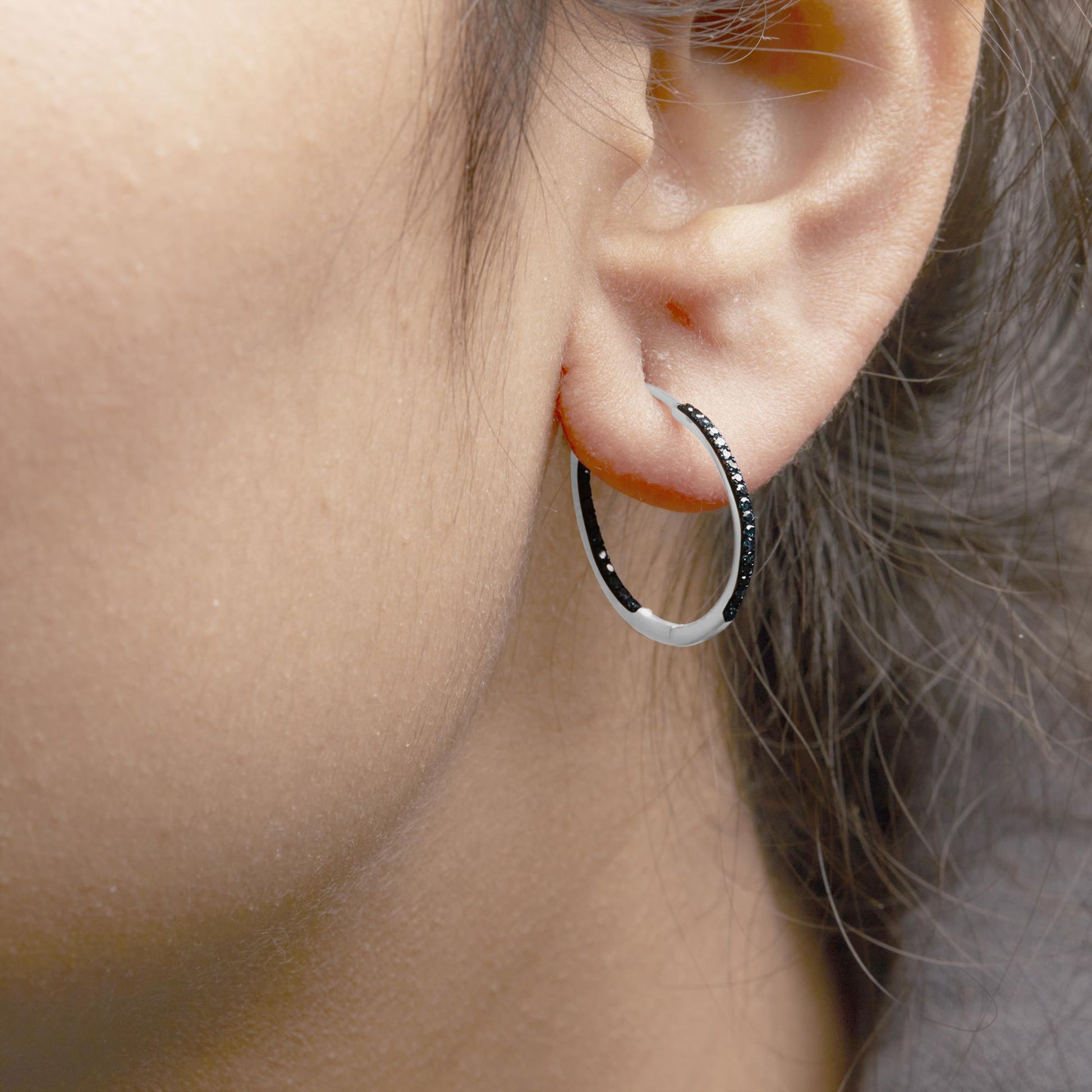 Close-up side view of a white metal hoop earring with prong-set round blue gemstones worn on a model's ear.