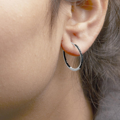 Close-up side view of a white metal hoop earring with prong-set round blue gemstones worn on a model's ear.