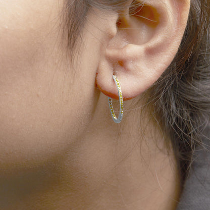 Close-up side view of a white metal hoop earring set with round yellow gemstones, worn on a model.