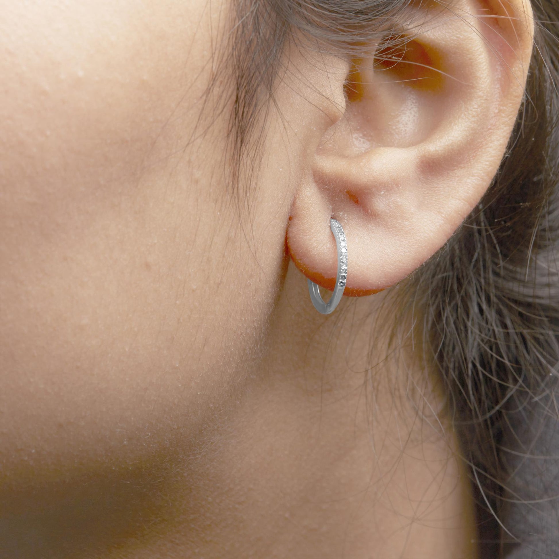 Close-up side view of a white metal hoop earring with round prong-set white gemstones, worn on a model.
