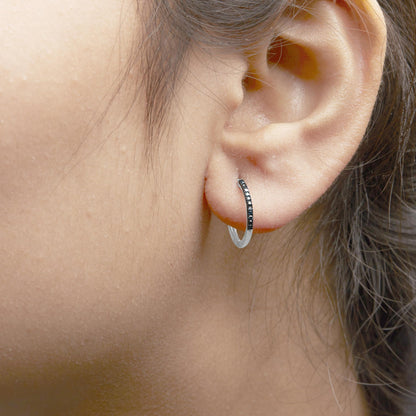 Close-up side view of a white metal hoop earring with round blue gemstones in prong settings, worn on a model's ear.