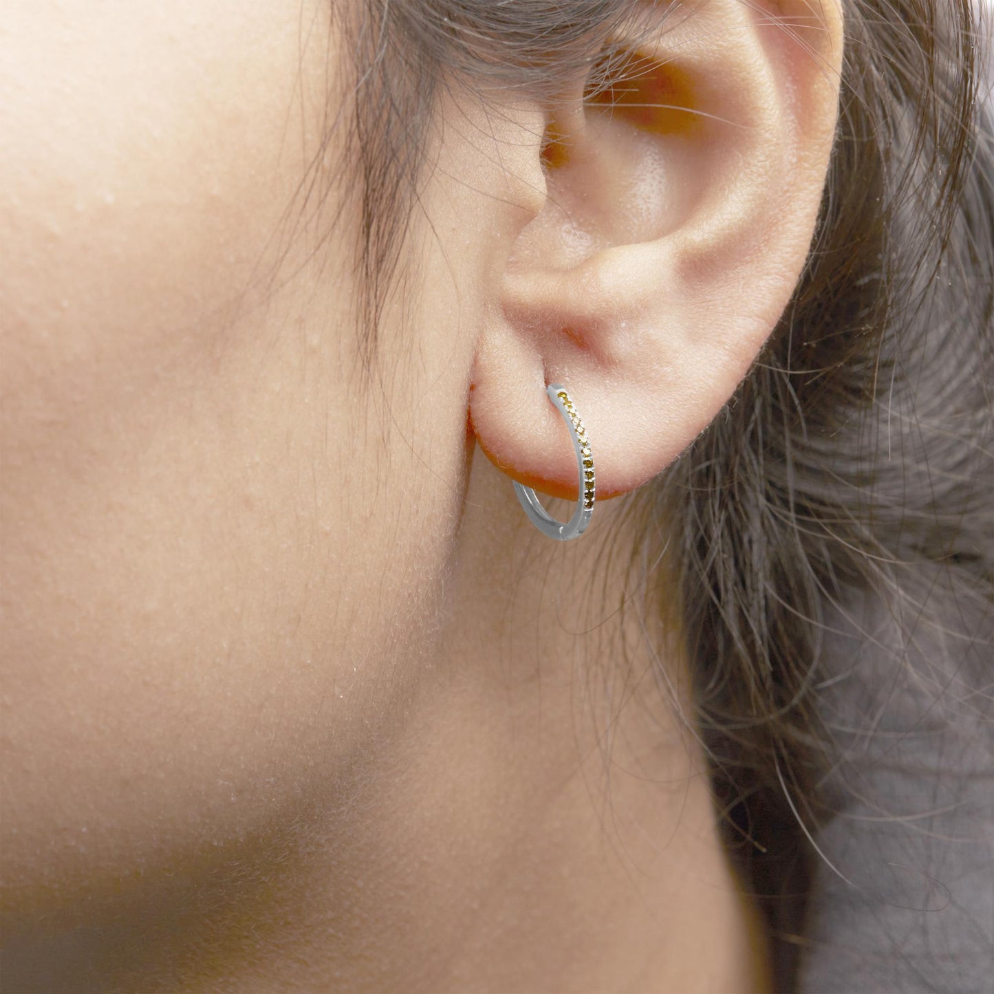 Close-up side view of a white metal hoop earring on a model's ear, adorned with round yellow gemstones in prong settings along the front.