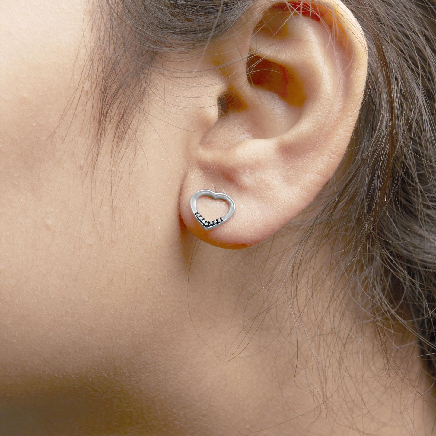 Close-up side view of a white metal heart-shaped earring with prong-set round blue gemstones at the bottom, worn on a model.