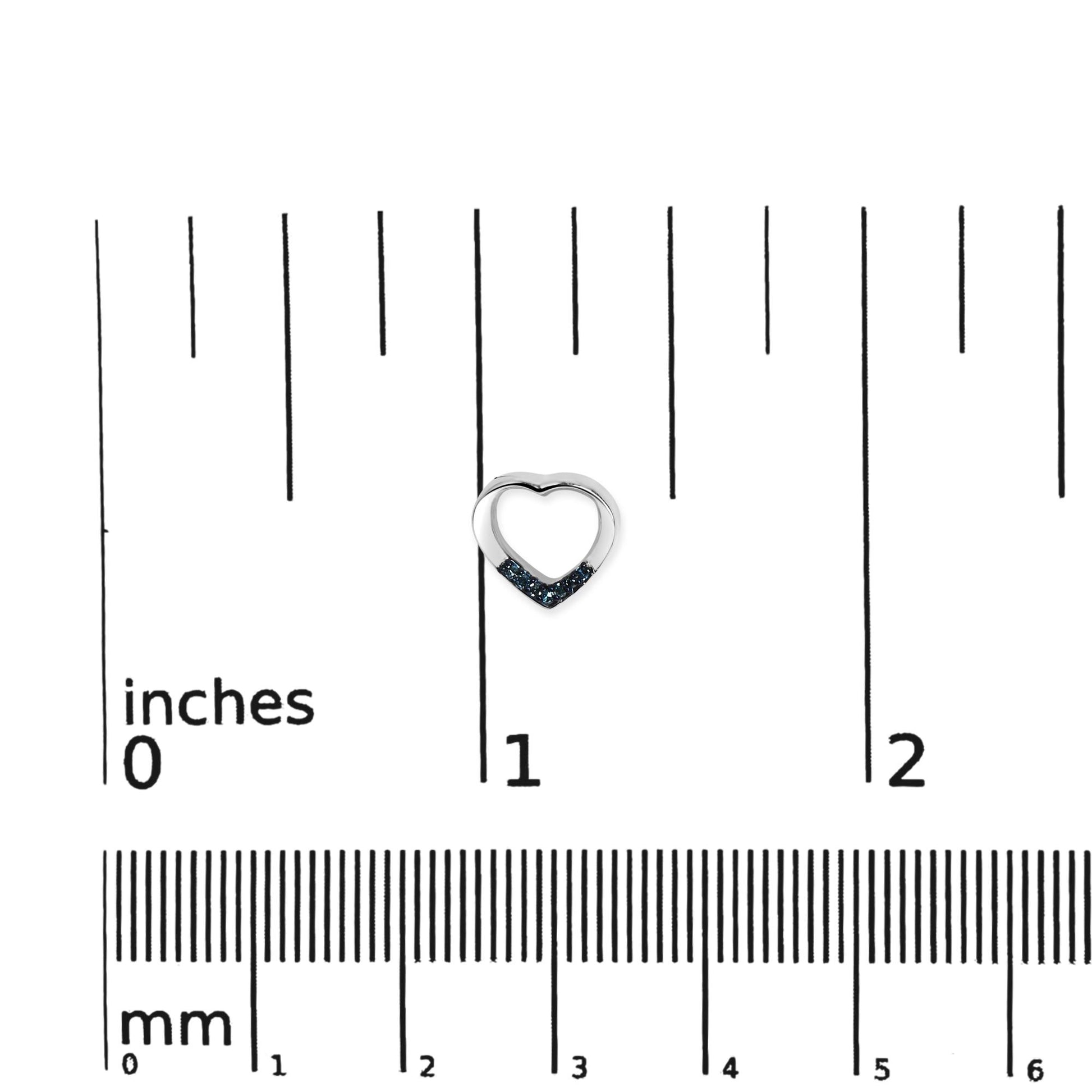 Close-up front view of a small white heart-shaped earring partially adorned with round blue gemstones, placed on a ruler for size reference.
