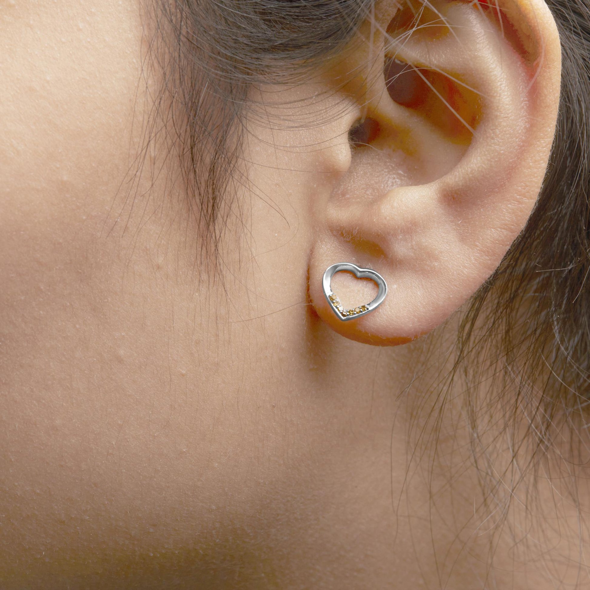 Close-up side view of a white metal open heart-shaped earring with small round yellow gemstones in prong settings, worn on a model's ear.