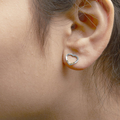Close-up side view of a white metal open heart-shaped earring with small round yellow gemstones in prong settings, worn on a model's ear.