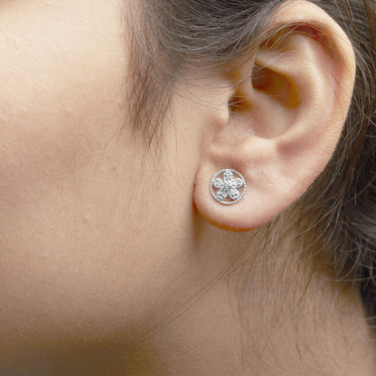 Close-up side view of a white metal flower-shaped earring with round prong-set white gemstones, worn on a model's ear.