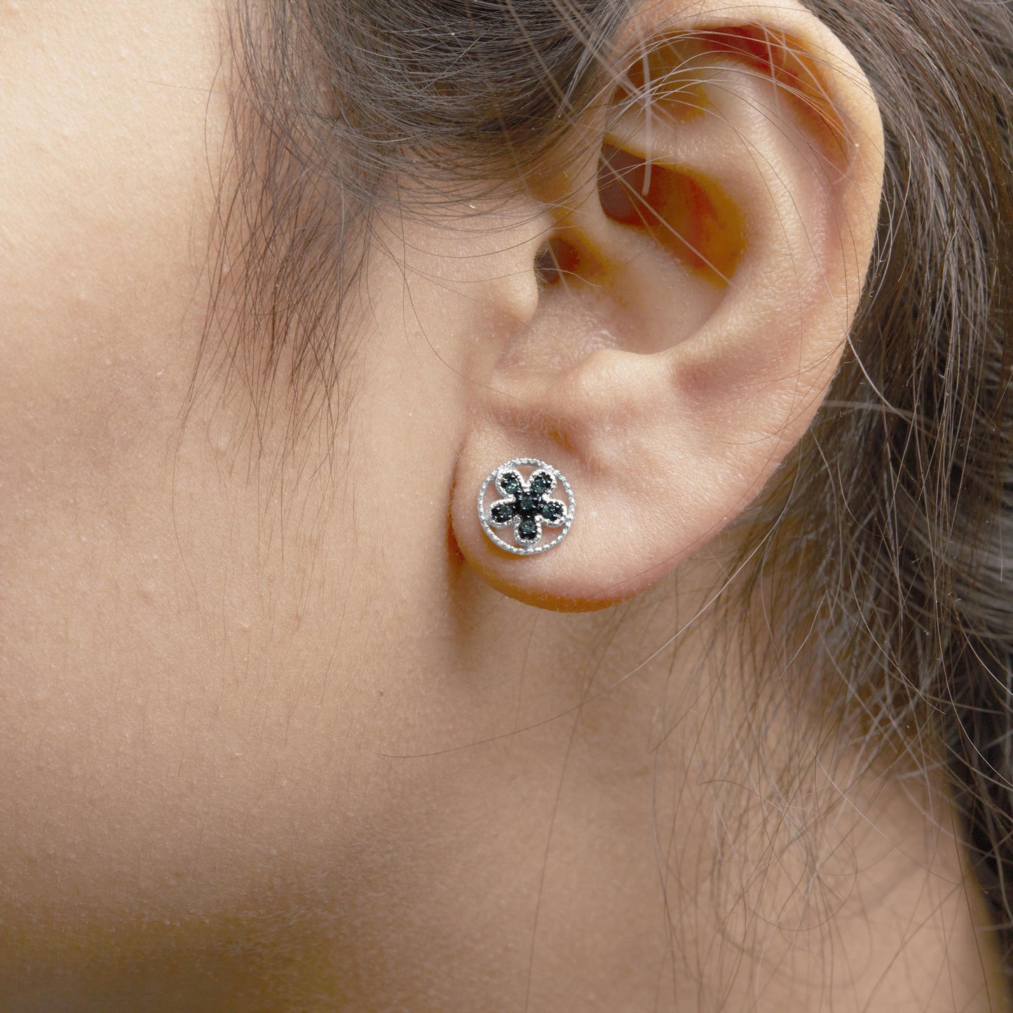Close-up side view of a white metal earring with a circular open design featuring multiple round blue prong-set gemstones, worn on a model's ear.