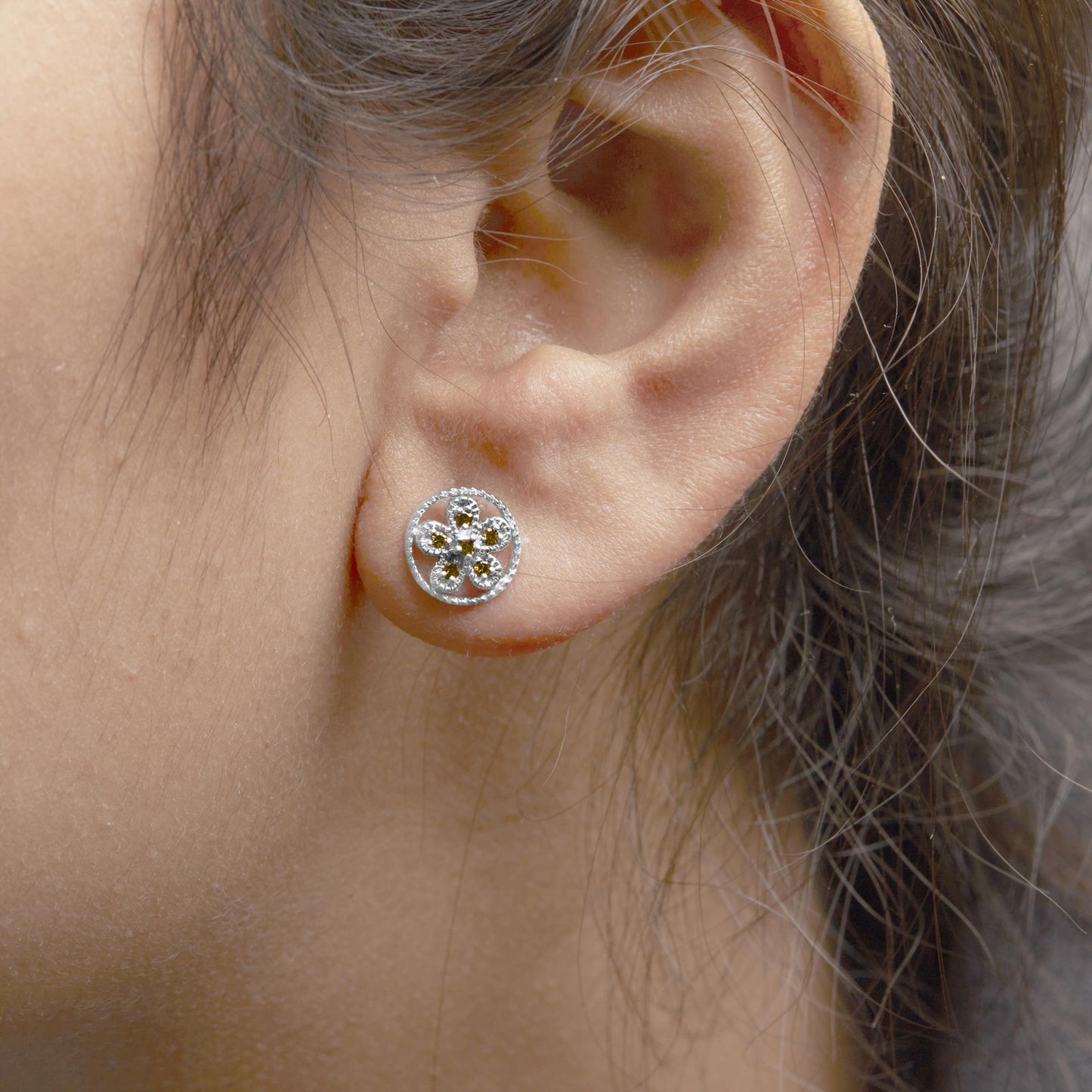 Close-up side view of a white metal round stud earring with yellow round gemstones in prong settings arranged in a floral pattern, worn on a model's ear.