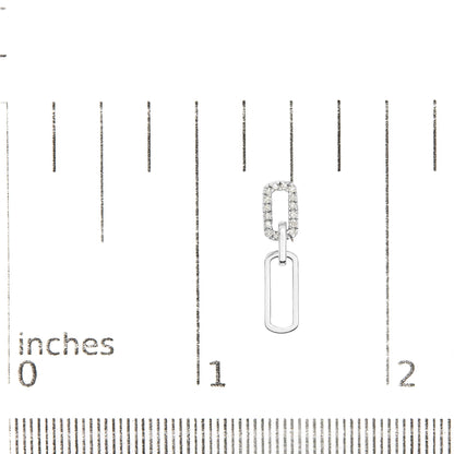 Close-up of white metal dangle earring with two linked geometric shapes, one encrusted with white gemstones, displayed on a ruler for size reference.