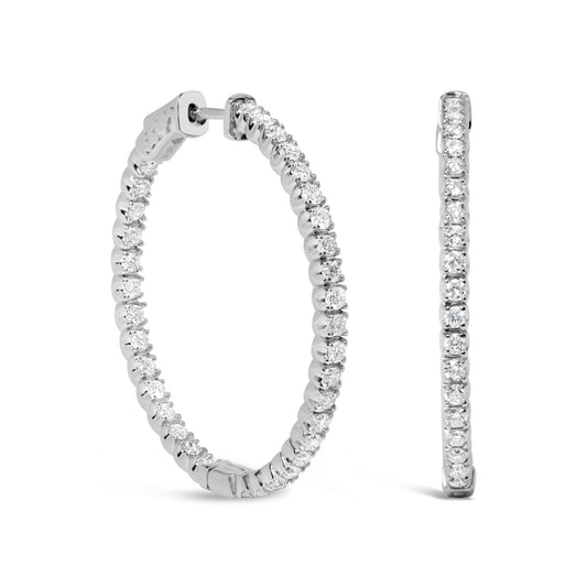 Side and front view of white metal hoop earrings set with round white gemstones in prong settings.