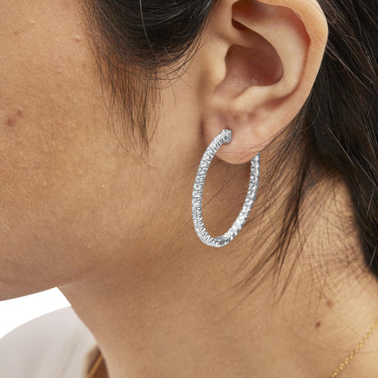 Close-up side view of a white metal hoop earring adorned with round white gemstones in prong settings, worn on a model.