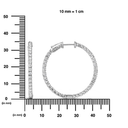 Pair of white metal hoop earrings with round white gemstones in prong settings, shown from side and front angles, displayed on a ruler for size reference.