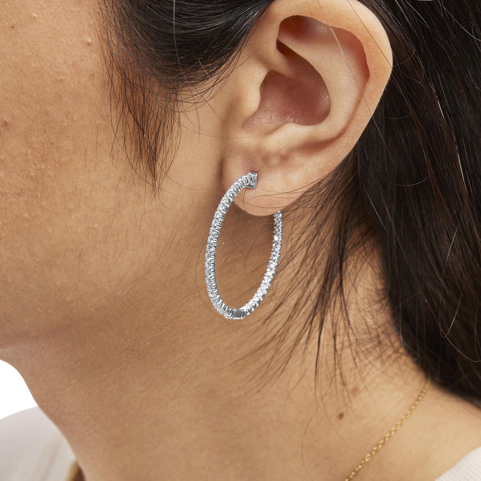 Close-up side angle of a model's ear wearing a white metal hoop earring adorned with round white gemstones in prong settings.