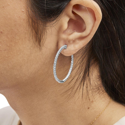 Close-up side angle of a model's ear wearing a white metal hoop earring adorned with round white gemstones in prong settings.