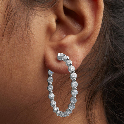 Close-up side view of a white metal hoop earring with round white gemstones in 2-prong settings, shown worn on a model.