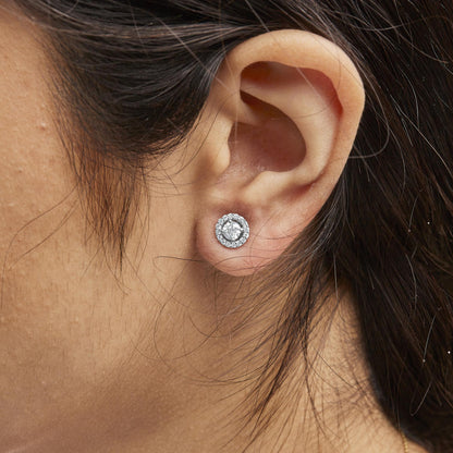 Close-up side view of white metal stud earring with a central round white gemstone surrounded by smaller round white gemstones, worn on a model's ear.