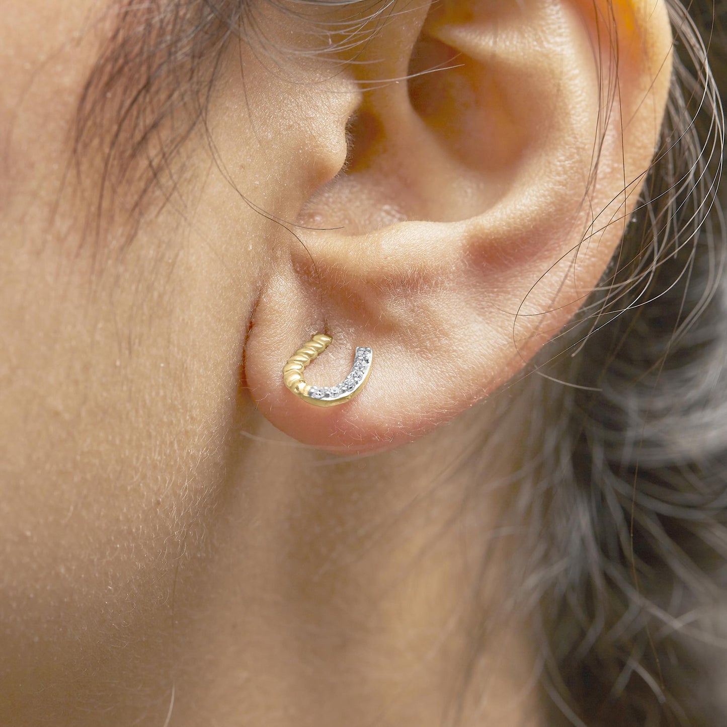 Close-up side view of a yellow metal earring on a model’s ear, featuring a curved design with half set with round white gemstones in prong settings.