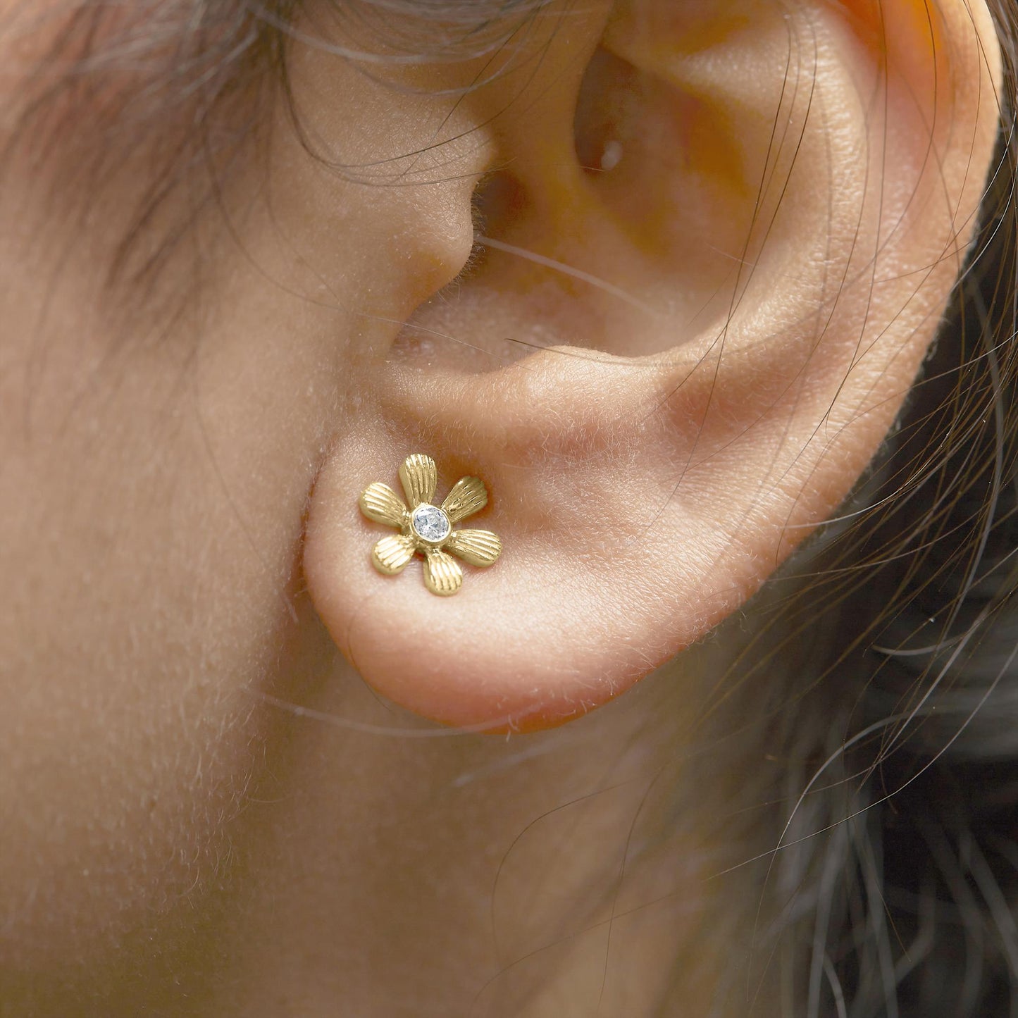 Close-up side view of a yellow metal flower-shaped earring with a round white gemstone in the center, worn on a model's ear.