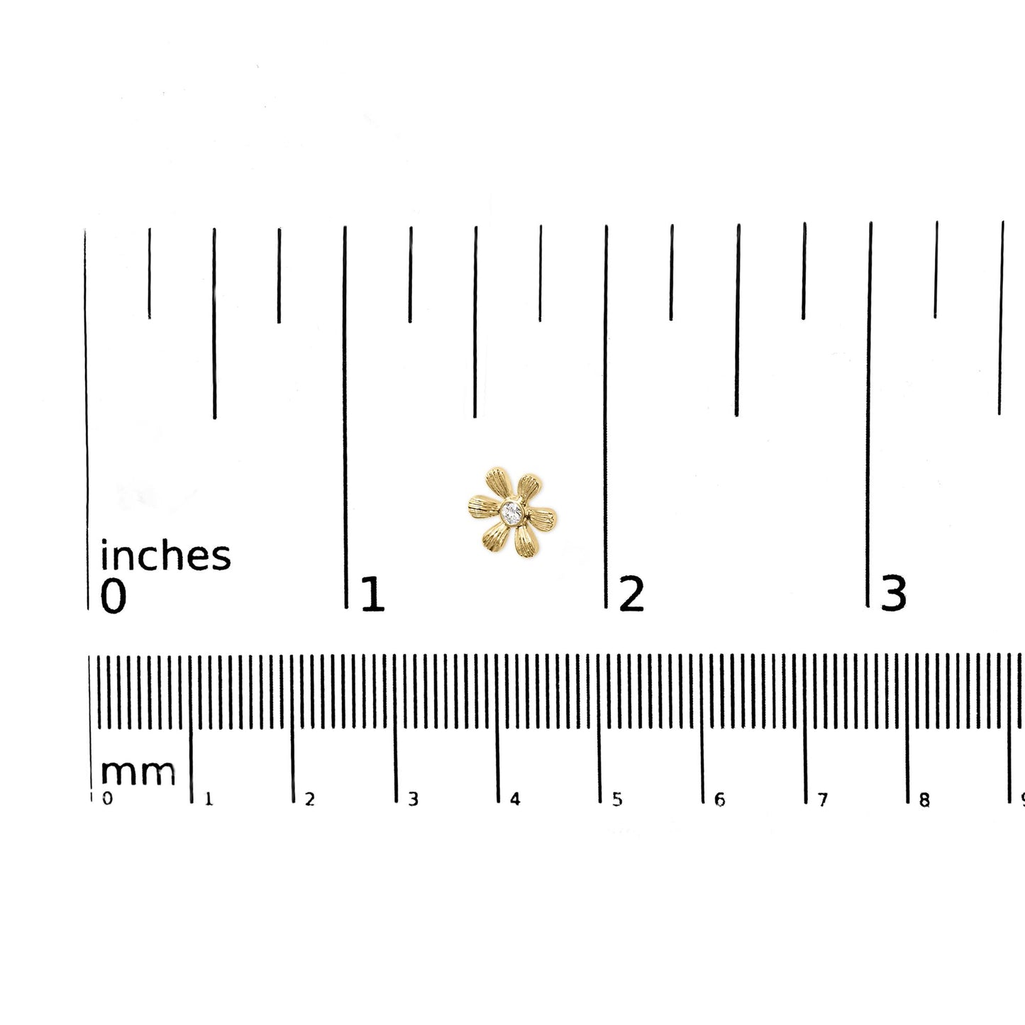 Close-up of a yellow metal flower-shaped earring with a round white gemstone in the center, placed on a ruler for size reference.