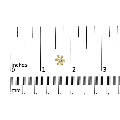 Close-up of a yellow metal flower-shaped earring with a round white gemstone in the center, placed on a ruler for size reference.