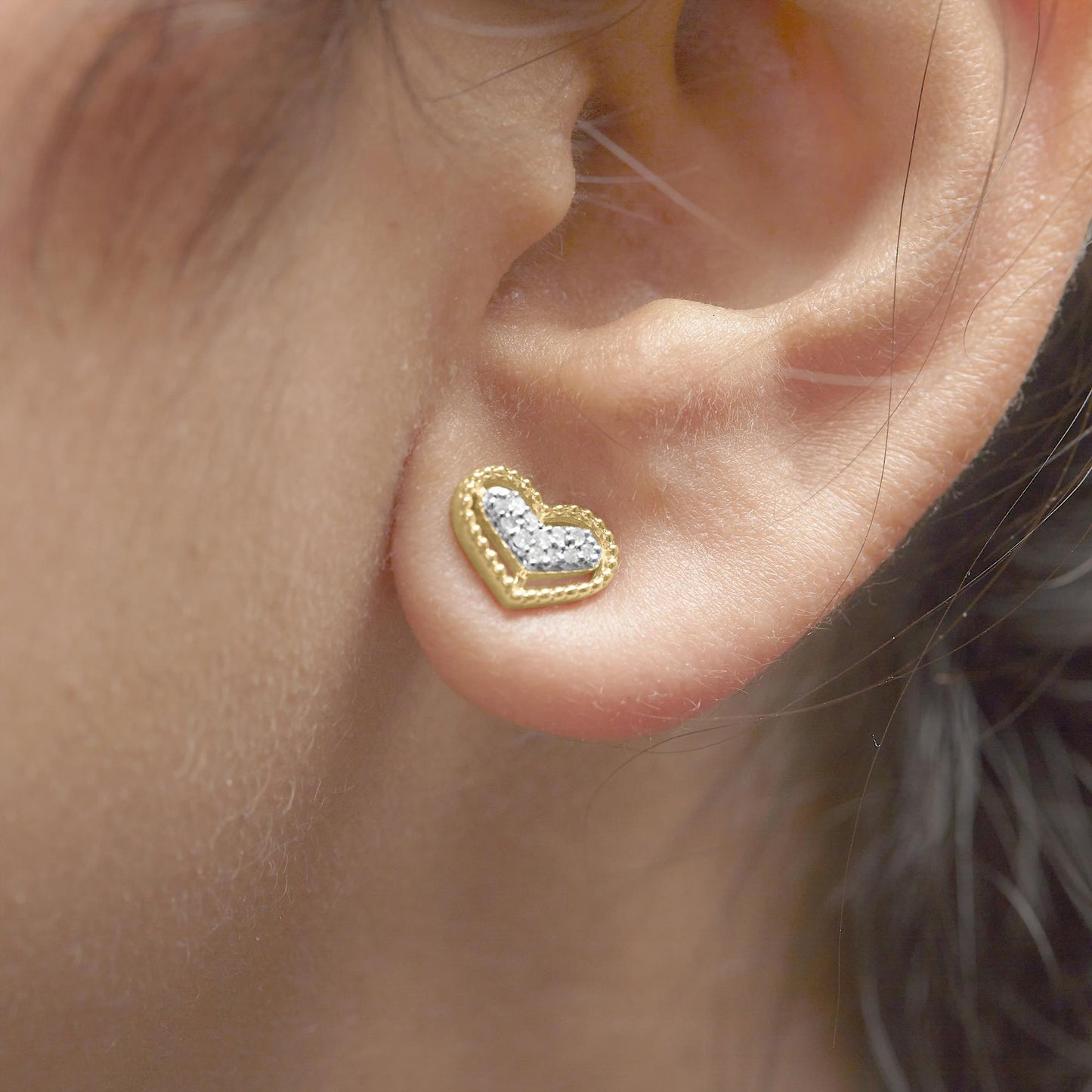 Close-up side view of a yellow metal heart-shaped earring with white round gemstones in a prong setting worn on a model's ear.
