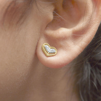 Close-up side view of a yellow metal heart-shaped earring with white round gemstones in a prong setting worn on a model's ear.