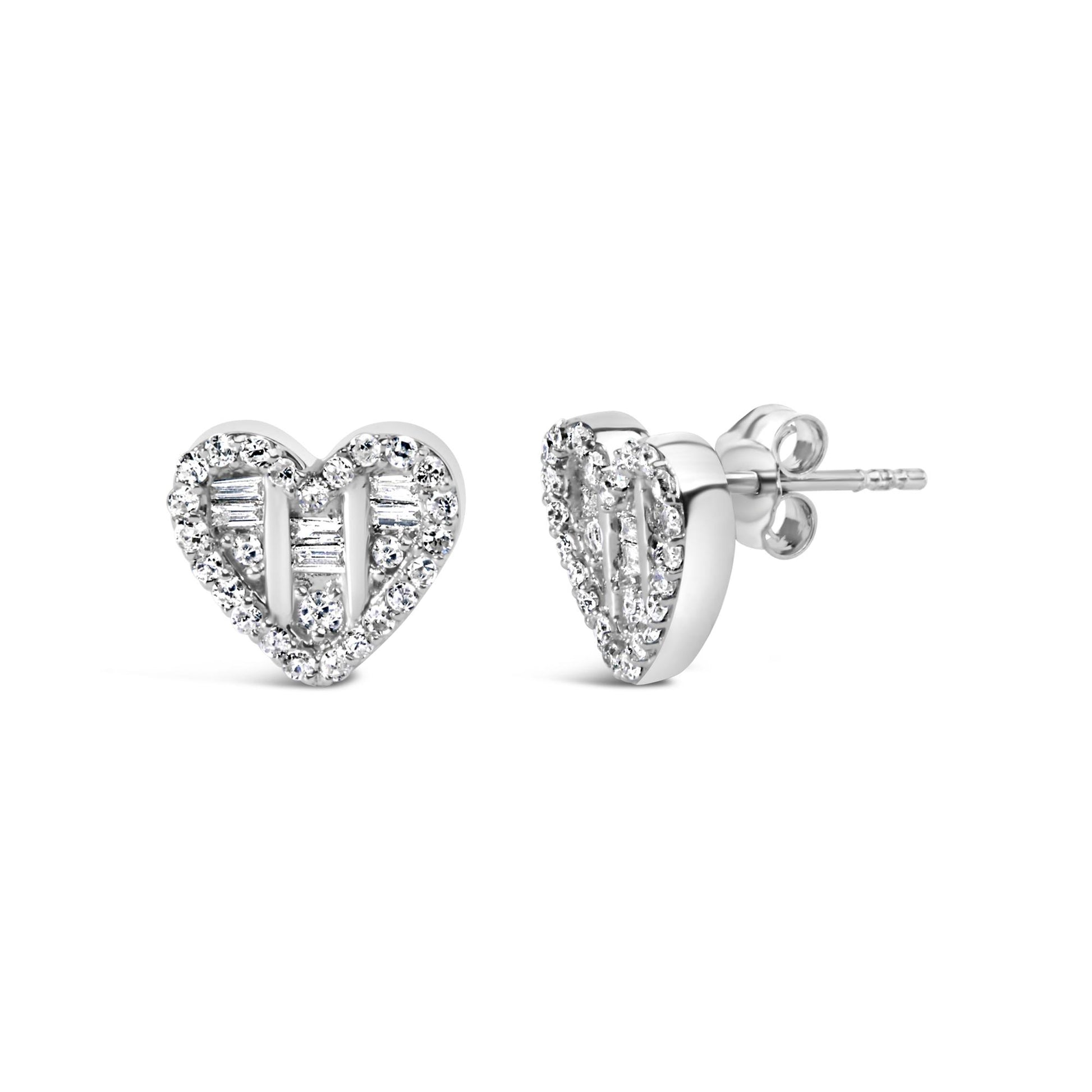 Front and side angle of white metal heart-shaped earrings studded with round and baguette white gemstones.
