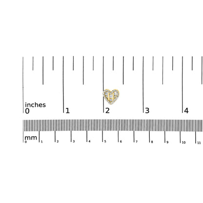 Close-up front angle of a yellow metal heart-shaped earring with round and baguette white gemstones in prong and channel settings, placed on a ruler for size reference.