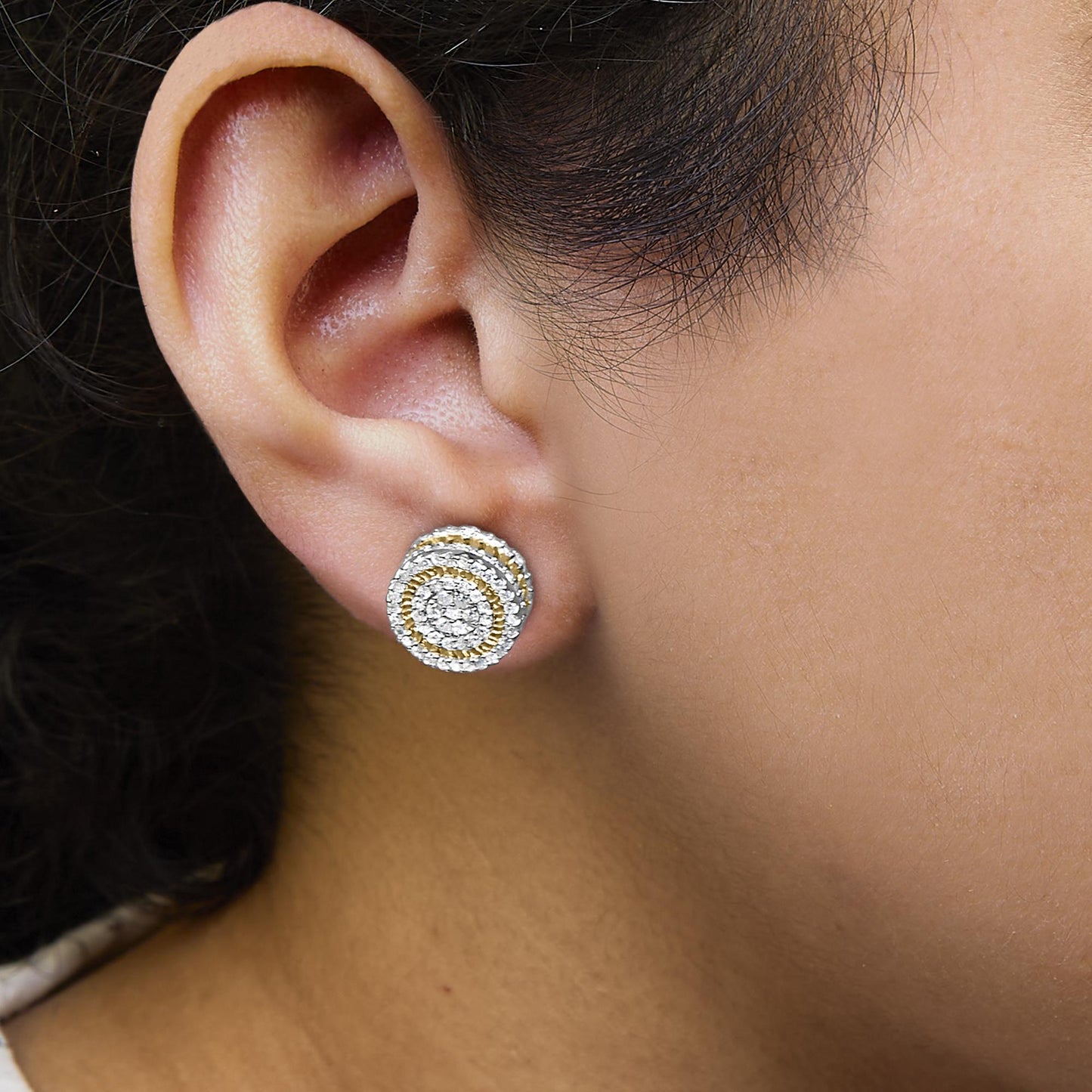 Close-up angled shot of a yellow metal earring with concentric circles of white gemstones in prong setting, worn on a model's ear.