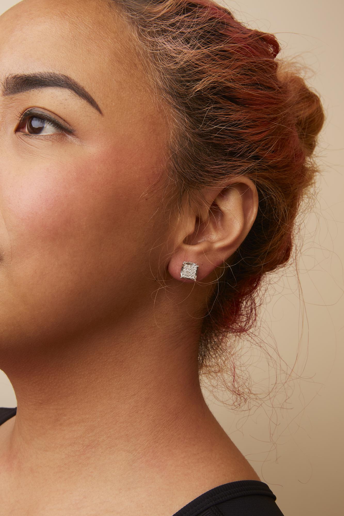 Close-up side angle of a model wearing white metal square stud earrings with multiple small white gemstones in prong settings.