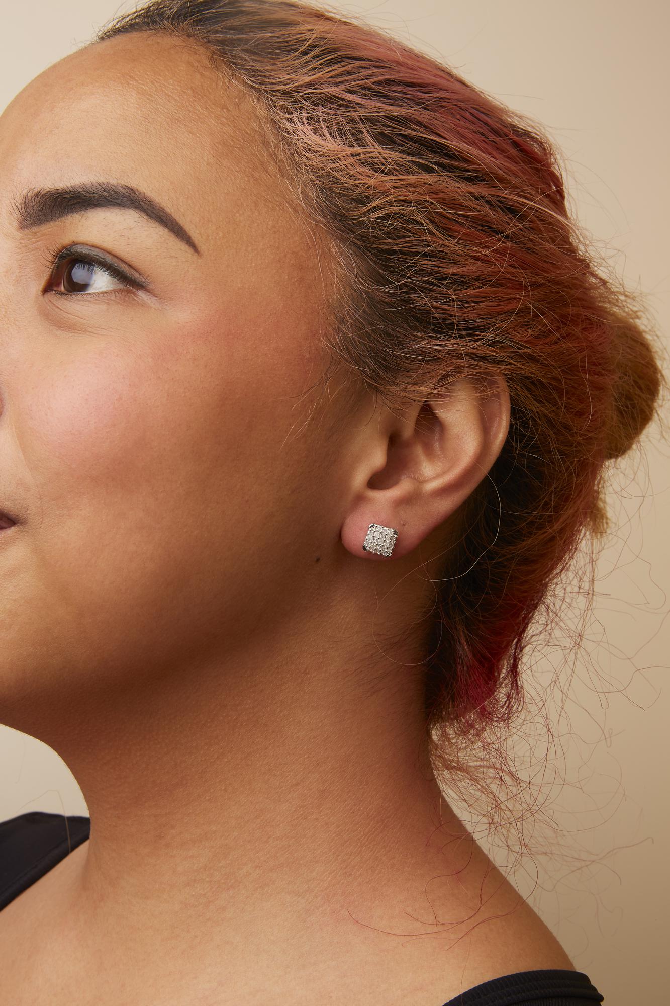Close-up side view of a model wearing white metal square stud earrings set with multiple princess-shaped white gemstones in prong settings.